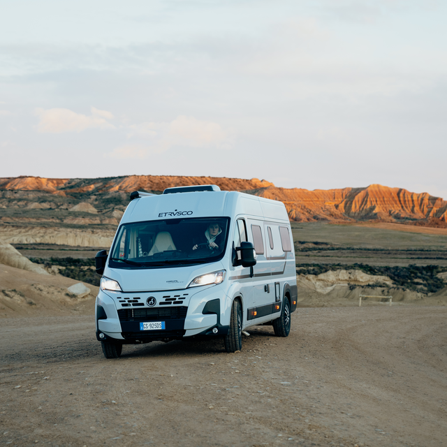 Moderner Etrusco Fiat Campervan Kastenwagen, fährt auf städtischer Straße vor Glasfassade, ideal für urbane Reisen.