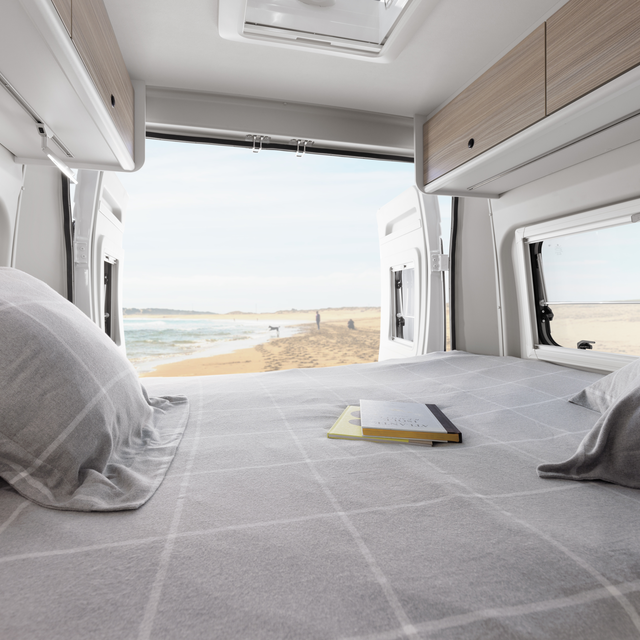 Moderner Innenraum eines Etrusco Campervan Fiat mit Wohnbereich, Doppelbett und Küstenblick durch ein großes Fenster - ideal fürs Camping.