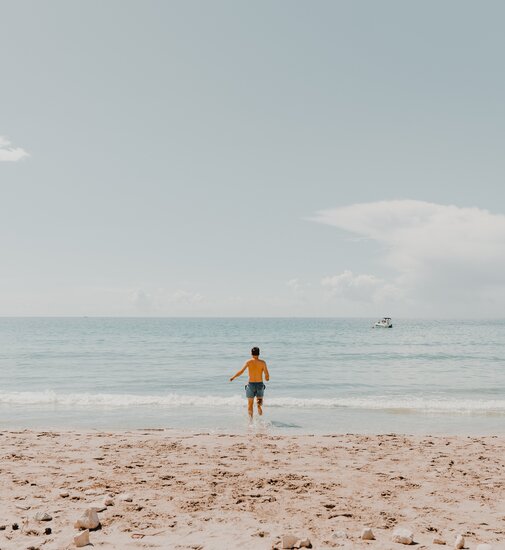 Man op het strand in een geel T-shirt en blauwe shorts loopt naar de zee tijdens een ontspannen kampeeruitje.