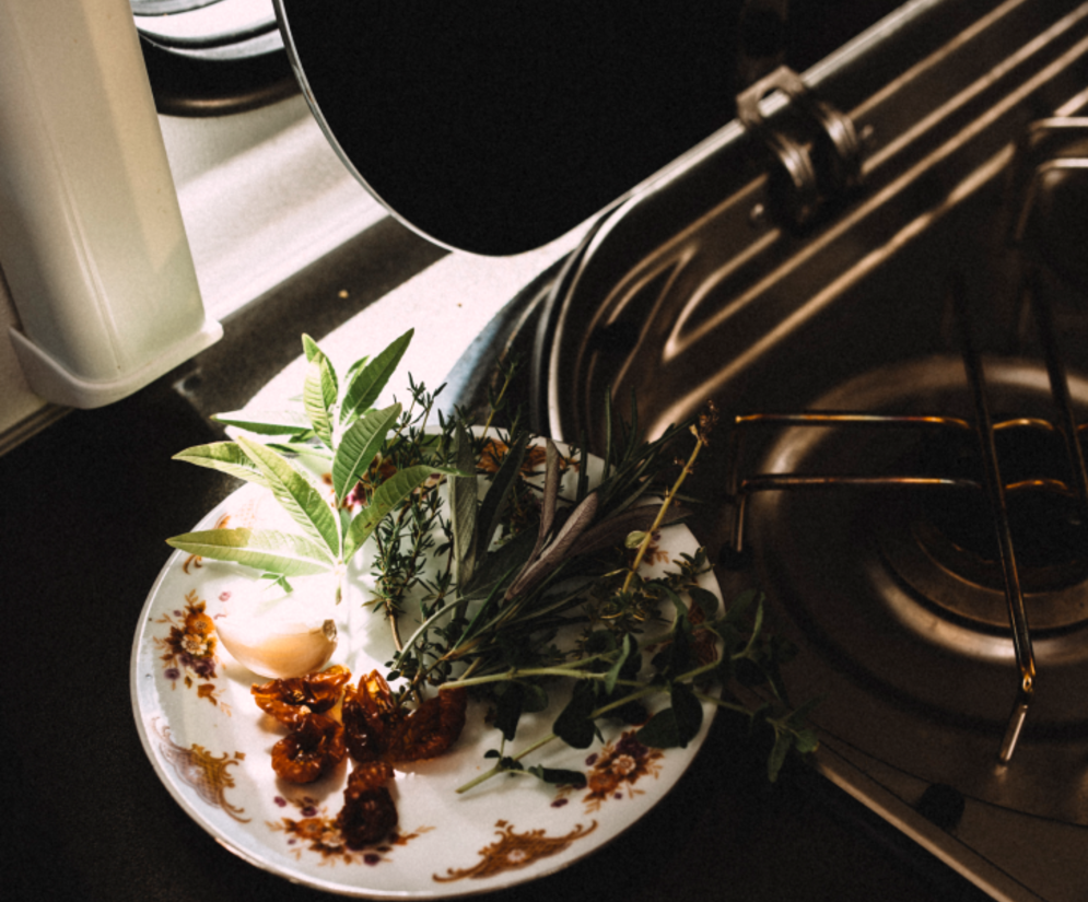 Cuisine d'un camping-car partiellement intégré Fiat d'Etrusco avec un réchaud à gaz, des herbes et des tomates sur une assiette, pour cuisiner confortablement en déplacement.