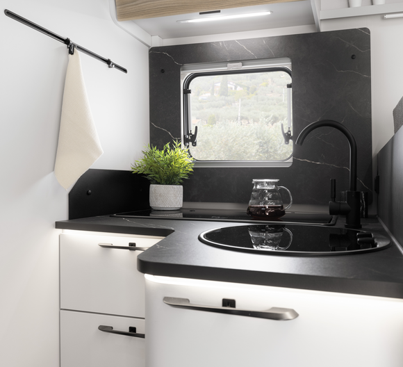 Cuisine d'un camping-car partiellement intégré Fiat d'Etrusco avec évier en acier inoxydable, réchaud à gaz fermé et lumière du jour par une fenêtre.