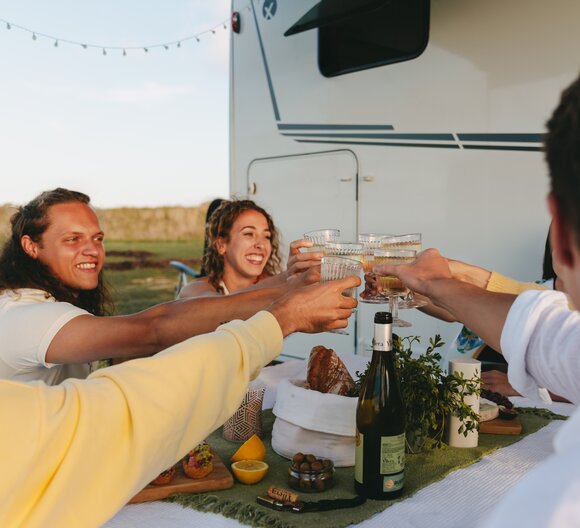 En gruppe venner skåler foran en Etrusco delintegreret autocamper Base T, mens de nyder et måltid på en campingplads.