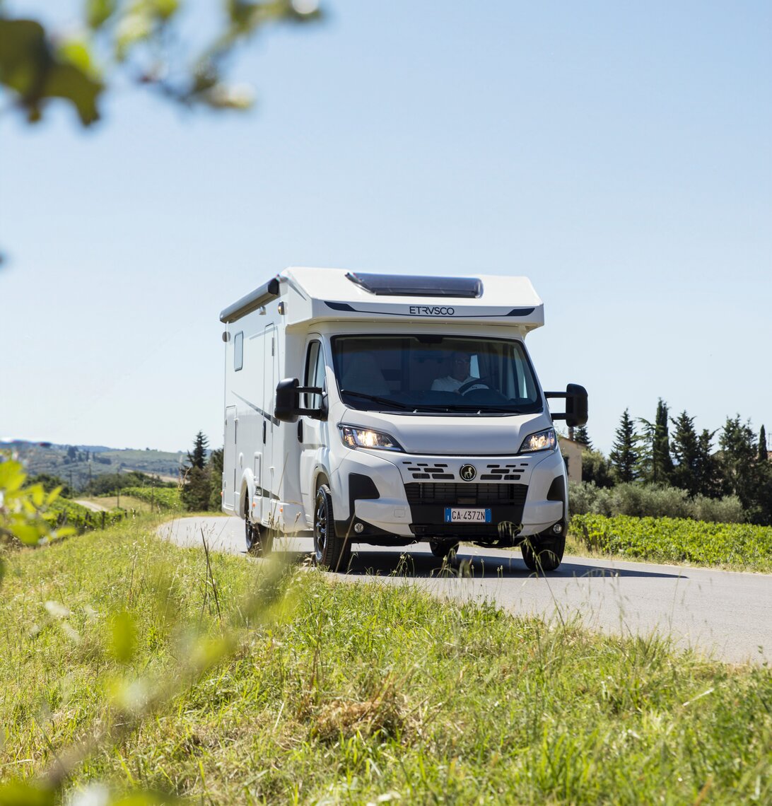 En Etrusco Base T delintegreret Fiat autocamper kører langs en malerisk vej, omgivet af oliventræer og stenmure.