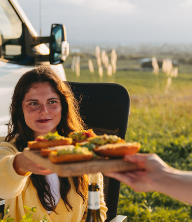 En kvinde sidder foran en Etrusco delintegreret autocamper på Ford-basis og serverer avocadobrød.