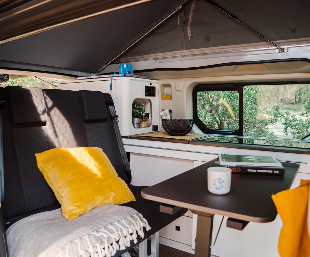 Interno accogliente di un Etrusco UC 5.0 XR Renault Urban Camper con tetto sollevabile, area salotto con cuscini e vista sulla cucina.