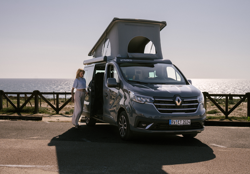 Etrusco UC 5.0 XR Renault Camper con tetto sollevabile in un parcheggio con vista sul mare, accanto una donna in abiti chiari.